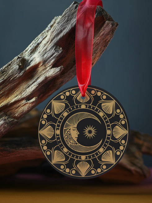Round metal ornament featuring a golden crescent moon face with star detail, surrounded by art deco shell motifs on black background. 3.5-inch diameter double-sided design with lunar phase pattern and crimson ribbon attachment. Vintage-inspired celestial artwork.